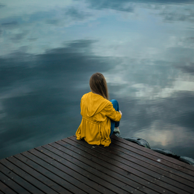 Woman sitting on a dock looking at water while struggling with finances