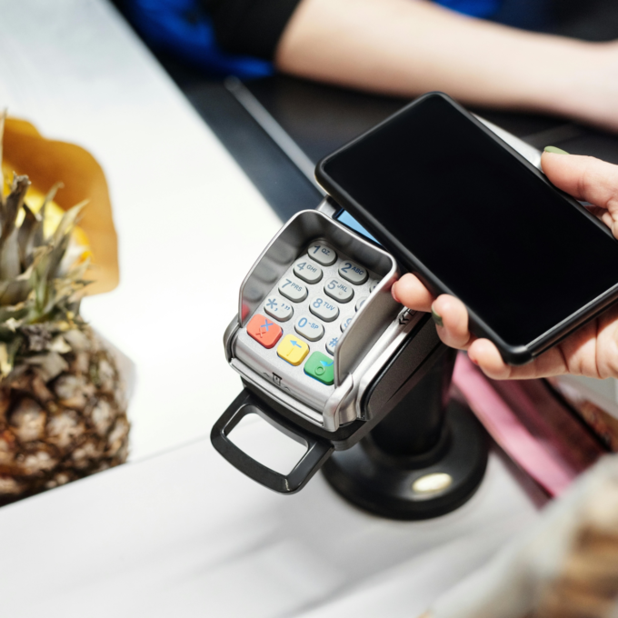 Person holding phone to card reader paying for groceries using credit