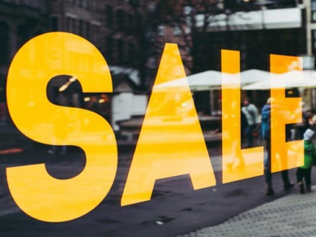 Yellow sale sign in storefront window urging shoppers to spend money