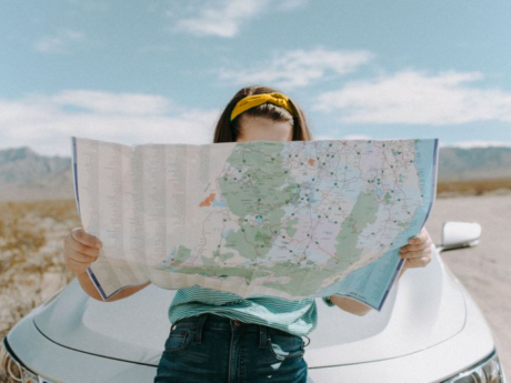 Woman on a budget friendly vacation seated on the hood of a car looking at a map
