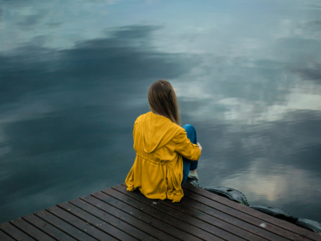 Woman sitting on a dock looking at water while struggling with finances