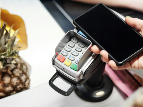 Person holding phone to card reader paying for groceries using credit