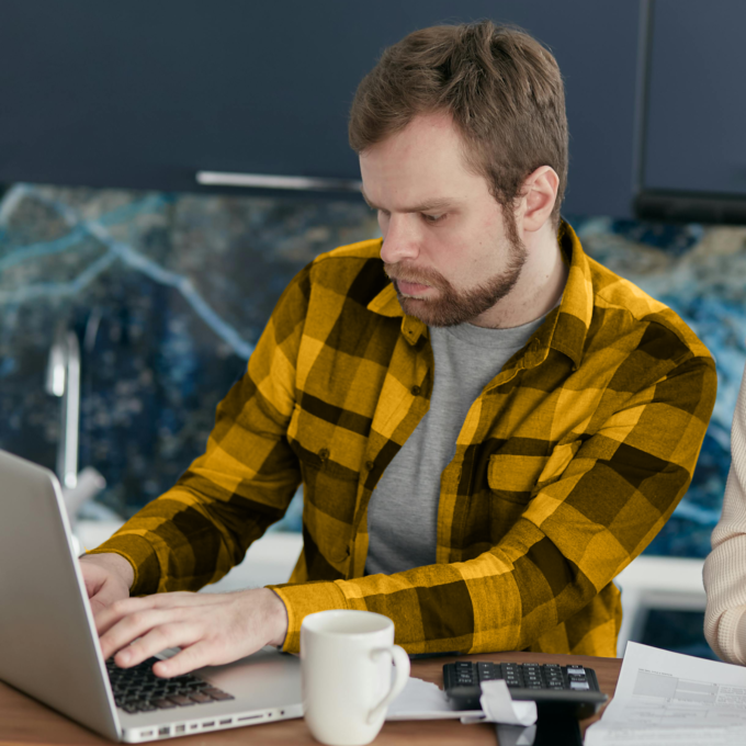 Man in a yellow shirt uses a laptop to review his budget.