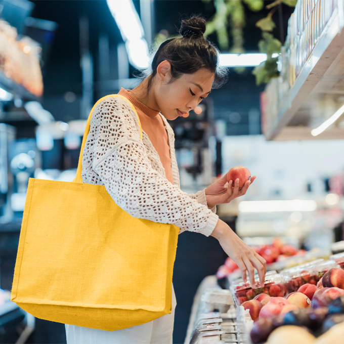 Young woman carrying a large yellow tote bag shopping for produce in a grocery store