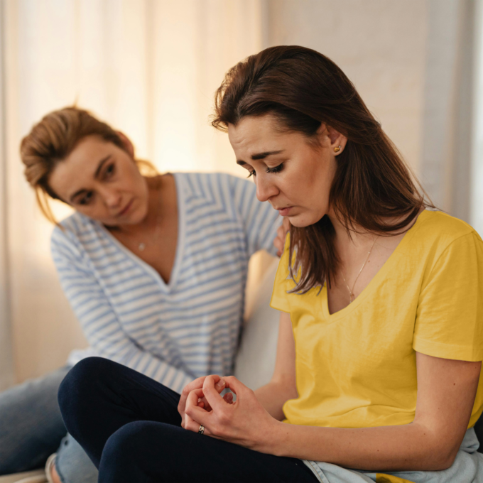 Sad woman sitting on couch being consoled by friend.