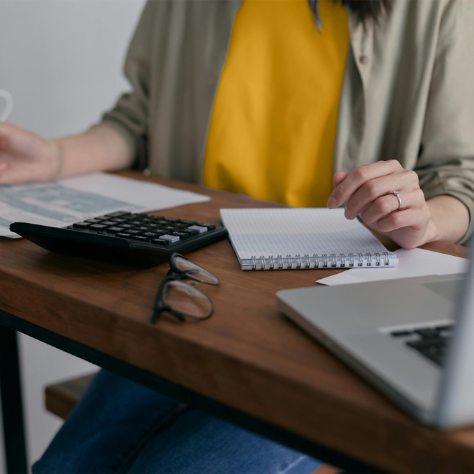 Person working at a desk with a laptop, calculator, and notepad.