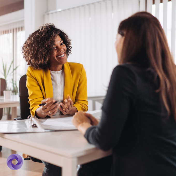Two people sit at a table reviewing documents, engaged in discussion in a professional office.