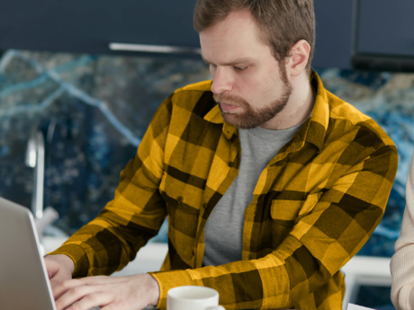 Man in a yellow shirt uses a laptop to review his budget.