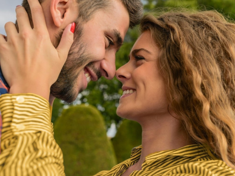 A man and woman hugging and smiling outside surrounded by trees