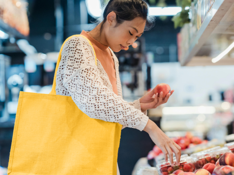 Young woman carrying a large yellow tote bag shopping for produce in a grocery store