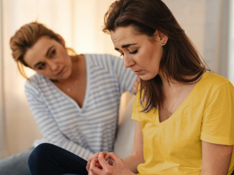 Sad woman sitting on couch being consoled by friend.