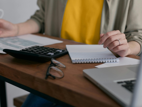Person working at a desk with a laptop, calculator, and notepad.
