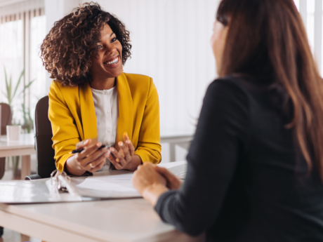 Two people sit at a table reviewing documents, engaged in discussion in a professional office.